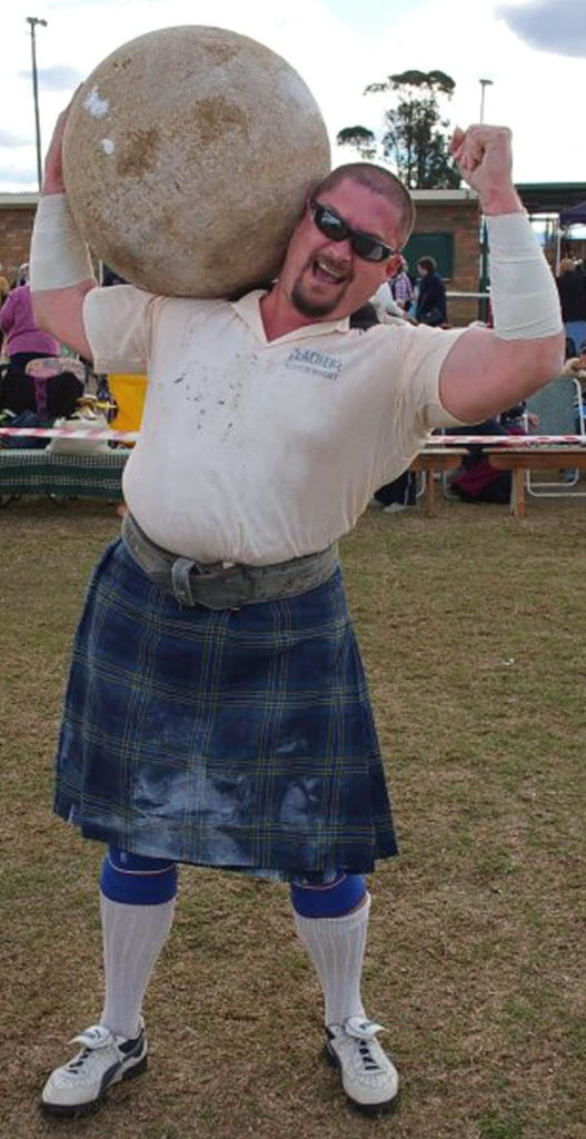 Sidonio the Strongman shown carrying a heavy round boulder